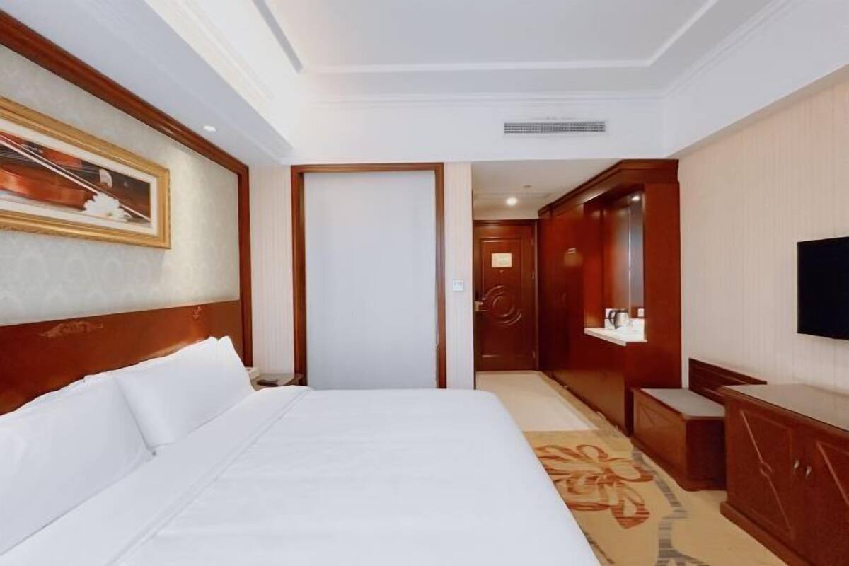 A hotel room with a large bed, a television, a wardrobe, and a door leading to another room.