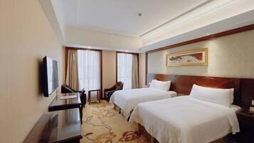 A hotel room with two beds, a desk, a chair, and a television.