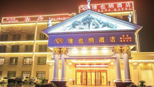 L’entrée d’un hôtel, avec une enseigne bien visible, une statue et une façade bien éclairée.