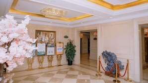 Un hall d'hôtel avec un sol à carreaux, un lustre, des tableaux encadrés posés sur des chevalets et une barrière en corde rouge.