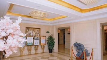 A hotel lobby with a checkered floor, a chandelier, framed pictures on easels, and a red rope barrier.
