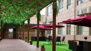 Une cour intérieure dotée d’un plancher en bois, d’une pelouse artificielle verte et de parasols rouges qui offrent de l’ombre.
