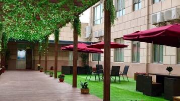 An indoor courtyard with a wooden floor, green artificial grass, and red umbrellas providing shade.