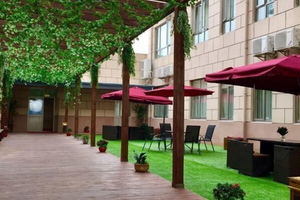 An indoor courtyard with a wooden floor, green artificial grass, and red umbrellas providing shade. - Vienna Hotel (Shanghai Wild Animal Park Metro Station) (Shanghai)