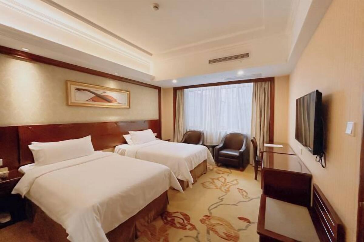 A hotel room with two beds, a desk, a chair, a television, and a window with curtains.
