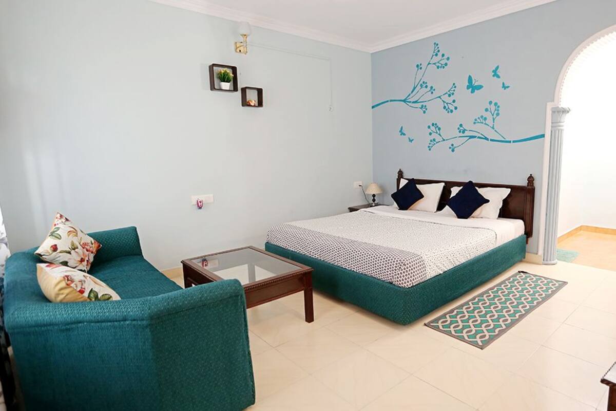 Um quarto com cama, sofá, mesinha e detalhe decorativo na parede.