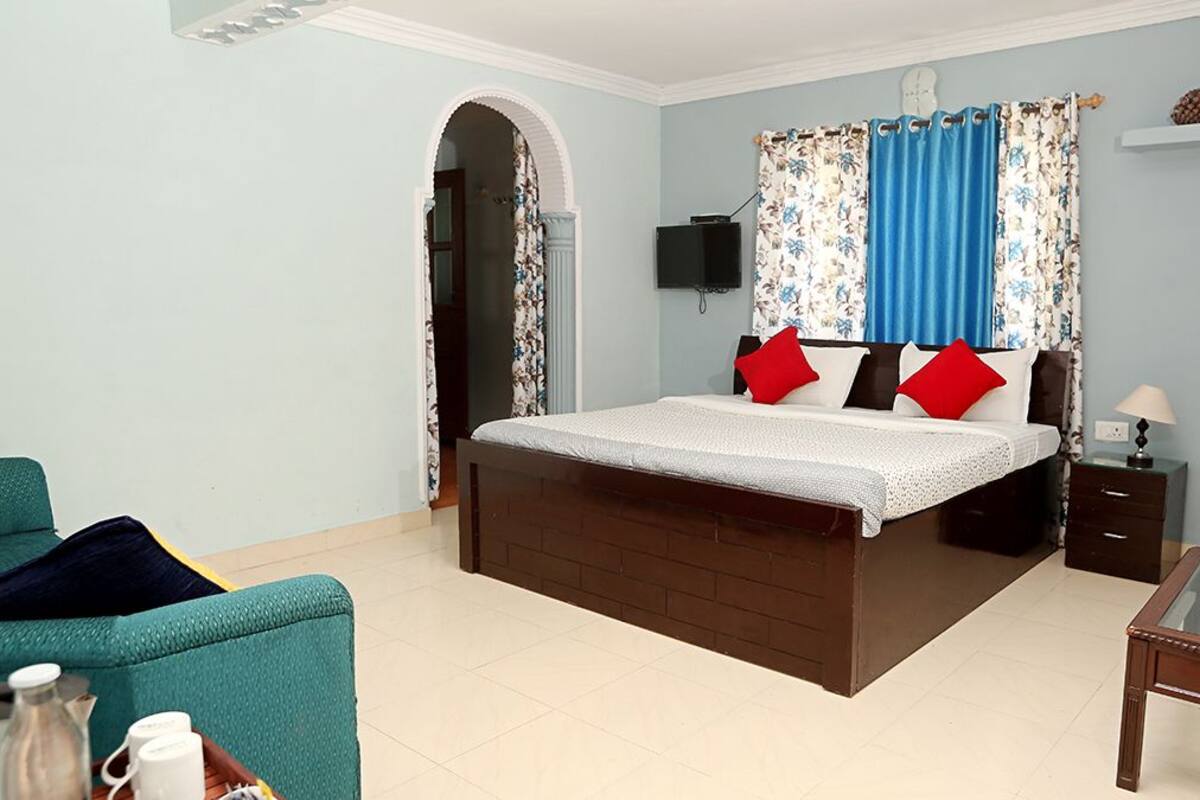 Quarto com cama, televisão, mesa de cabeceira, luminária e uma pequena mesa.