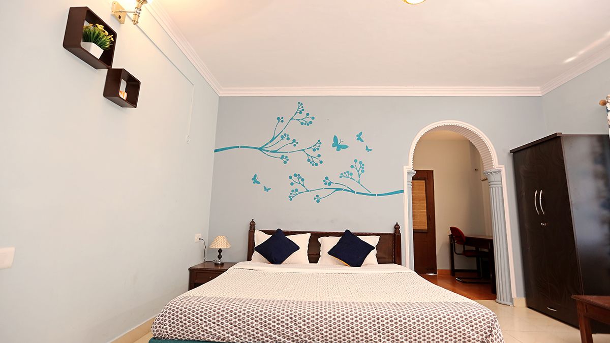 Een slaapkamer met een bed, nachtkastje, dressoir en een muur met een sticker van een tak en vlinder.