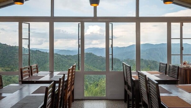 Un espace repas avec des tables et des chaises, de grandes fenêtres et des luminaires suspendus.
