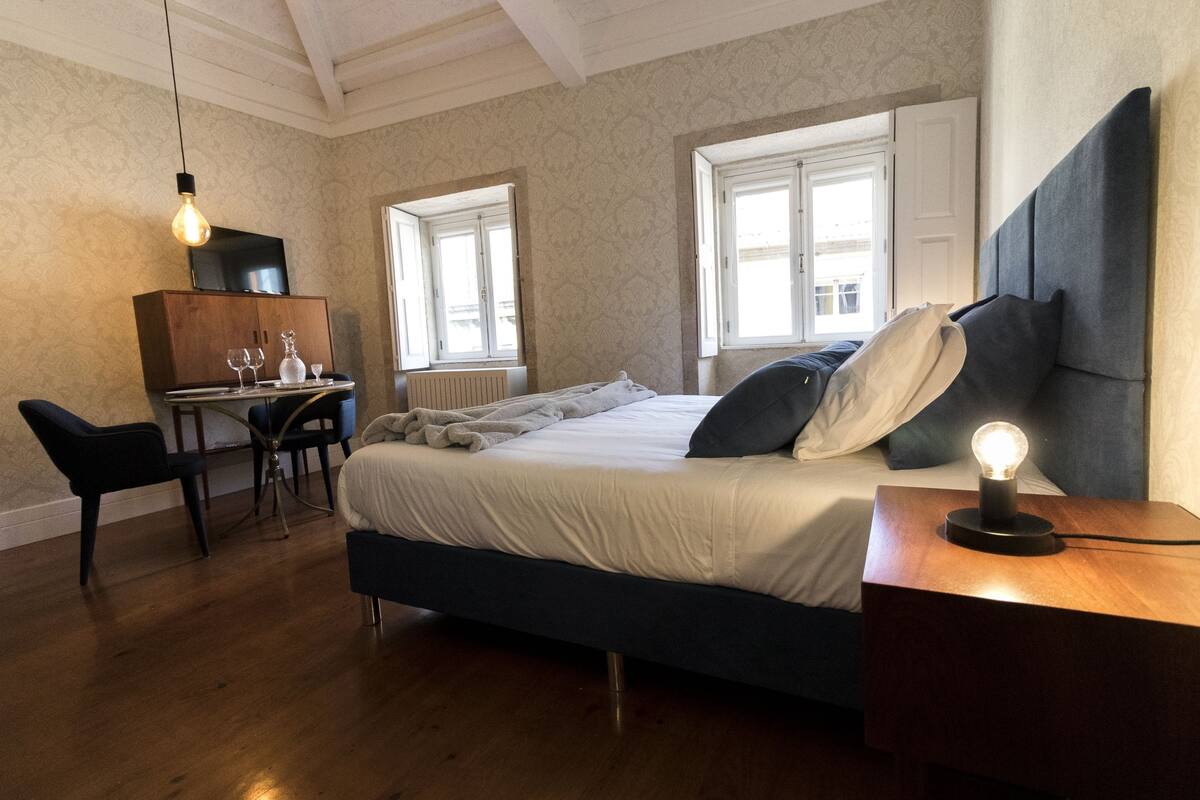 A bedroom with a bed, bedside table, lamp, desk, chairs, and a television.