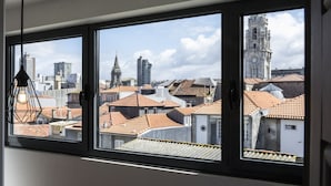 A view through a window with a metal frame, featuring a cityscape with buildings, a clock tower, and a clear sky. - Casa da Picaria (Porto)