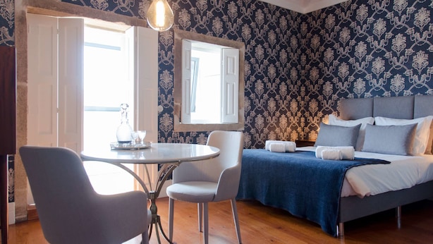 A room with a bed, a table with chairs, a mirror, and a patterned wallpaper. - Casa da Picaria (Porto)
