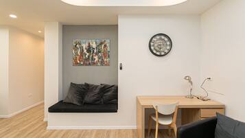 A modern room with a wooden desk, a white chair, a black couch, and a wall clock.