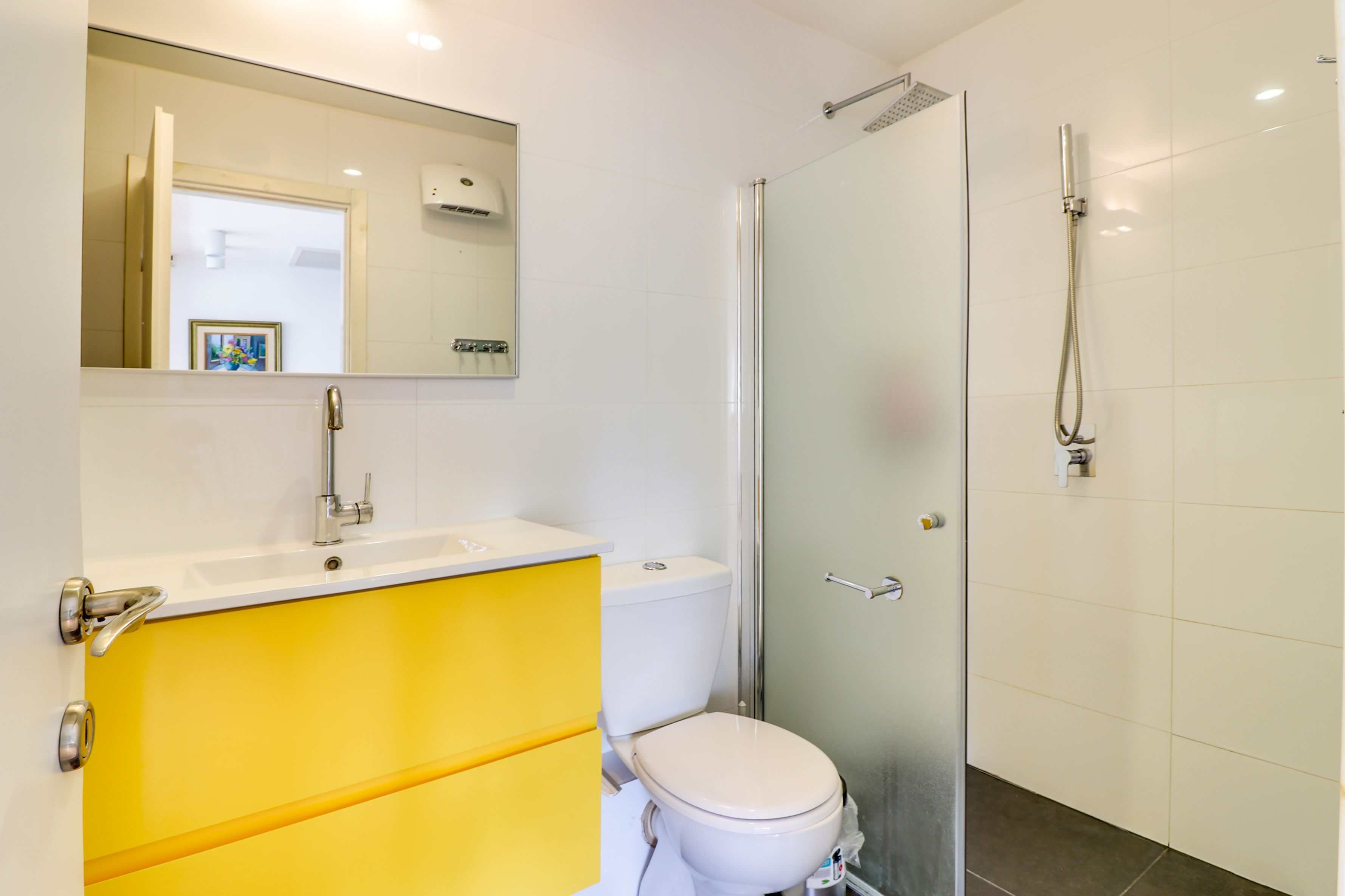 Et badeværelse med en guldfarvet kommode, et hvidt toilet, en brusekabine i glas og et spejl over vasken.