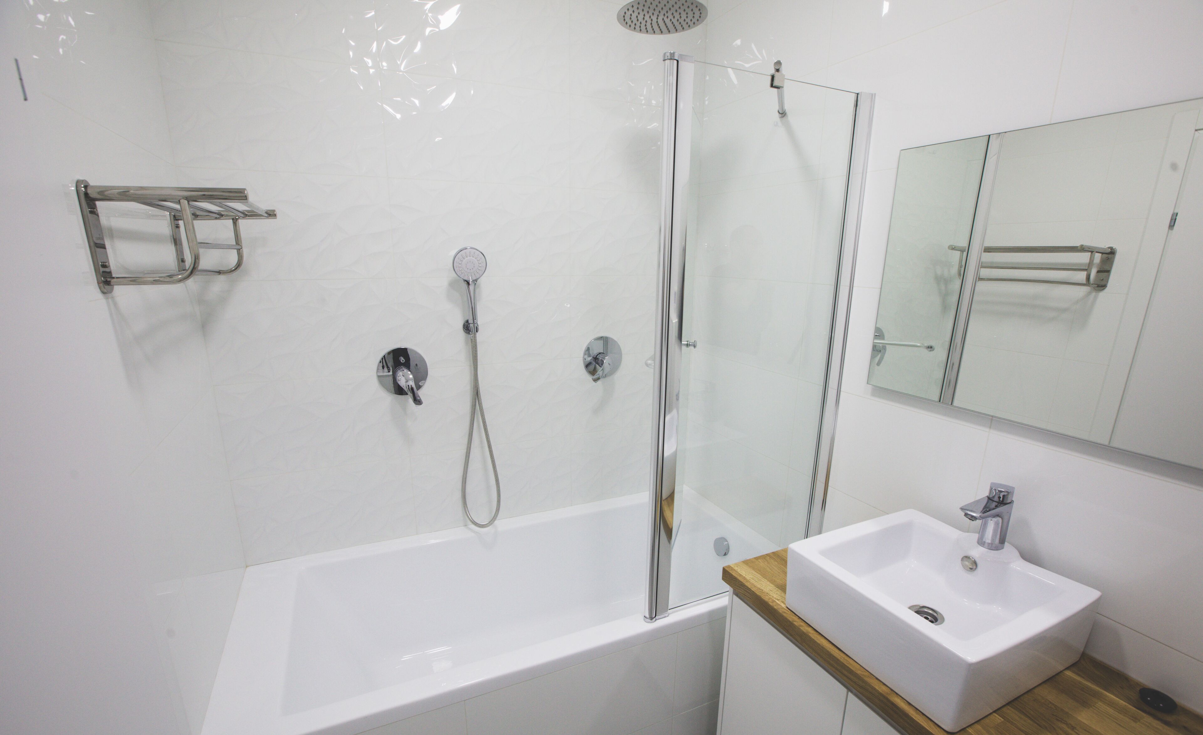 A modern bathroom with a glass-enclosed shower, a white bathtub, and a wooden vanity with a sink.