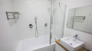 A modern bathroom with a glass-enclosed shower, a white bathtub, and a wooden vanity with a sink.