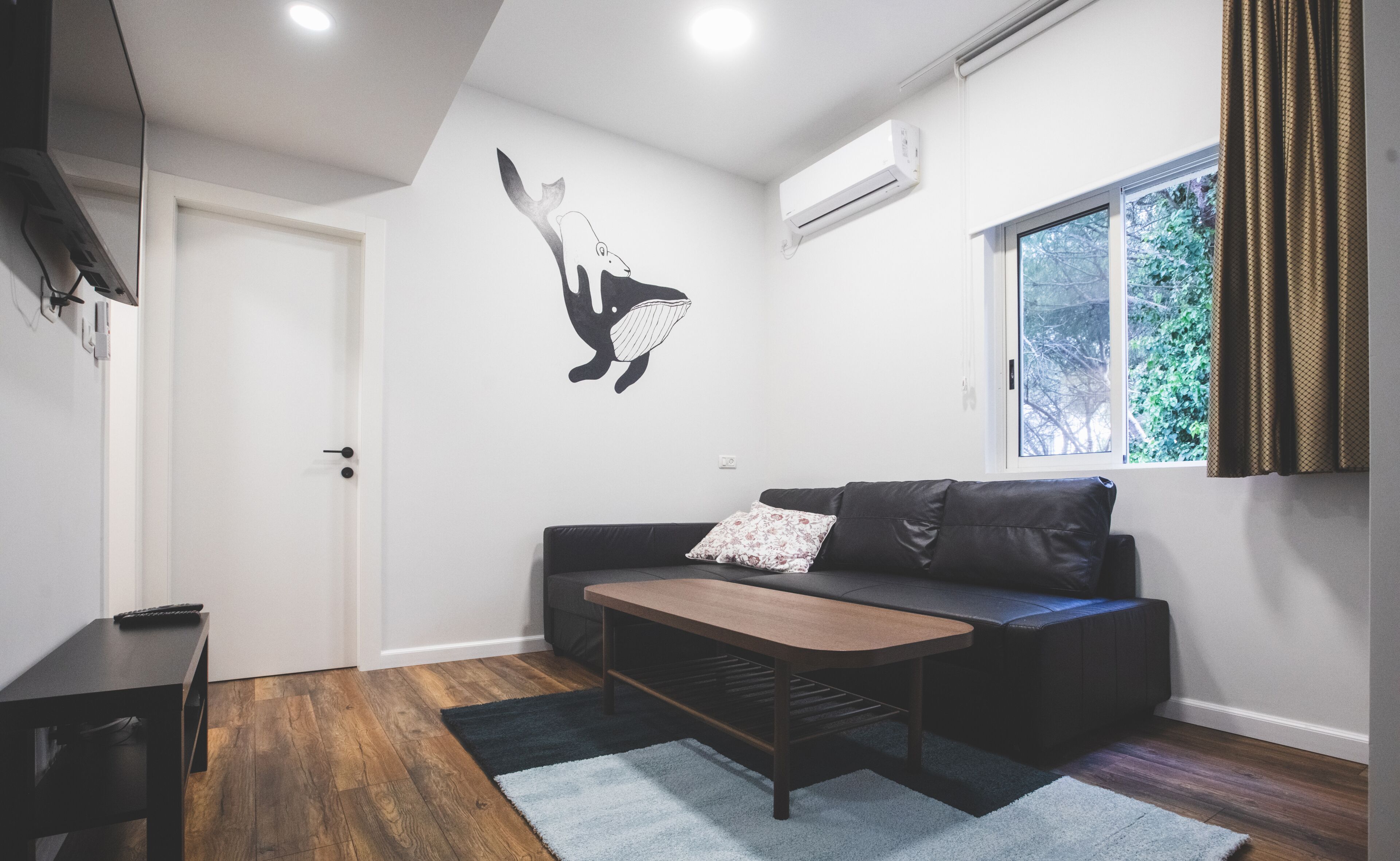Een moderne woonkamer met een leren zwarte bank, een houten salontafel en een luchtverwarmer aan de muur.