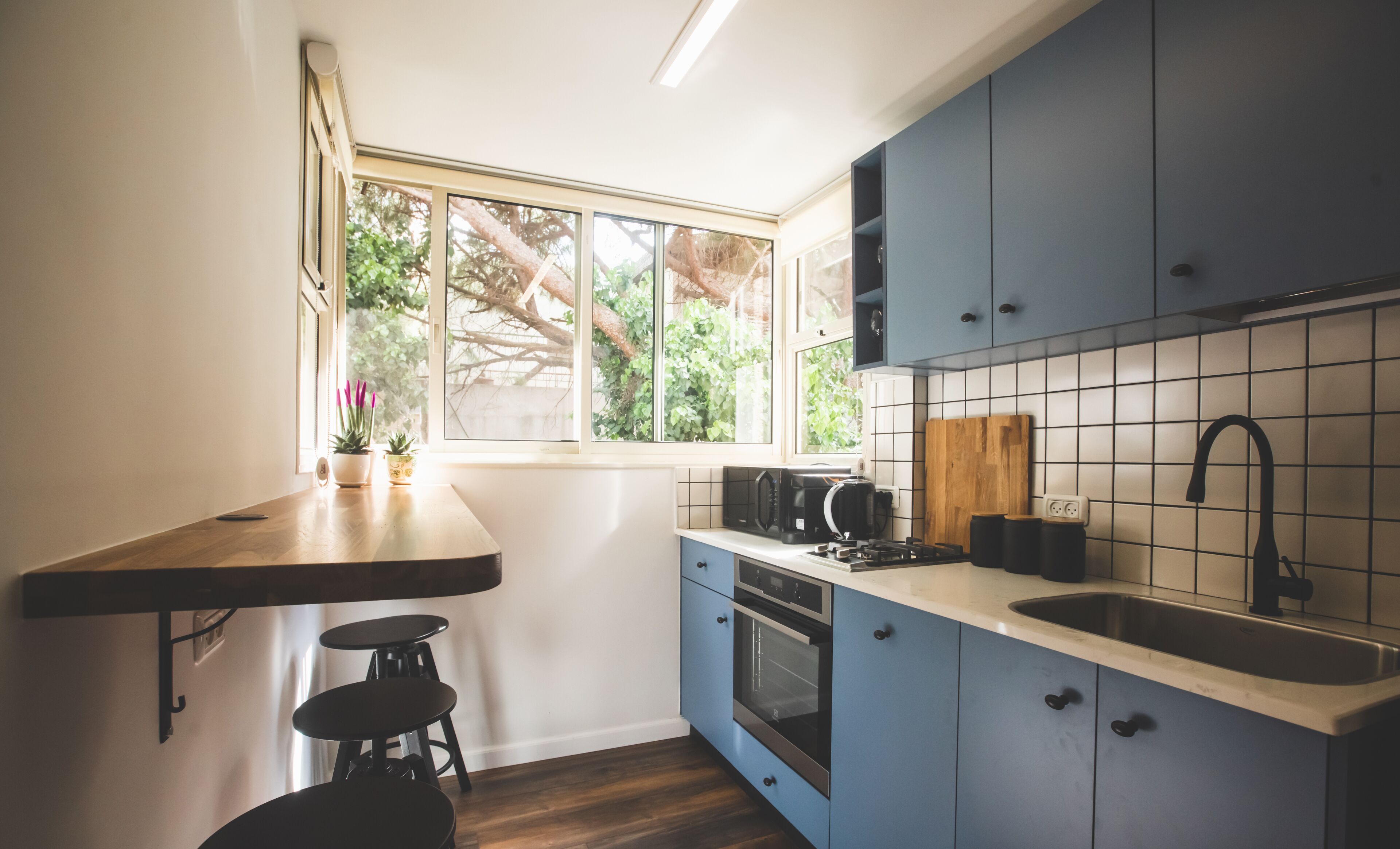 Une cuisine moderne avec des armoires bleues, un plan de travail en bois, un four encastré et une fenêtre donnant sur un paysage verdoyant.