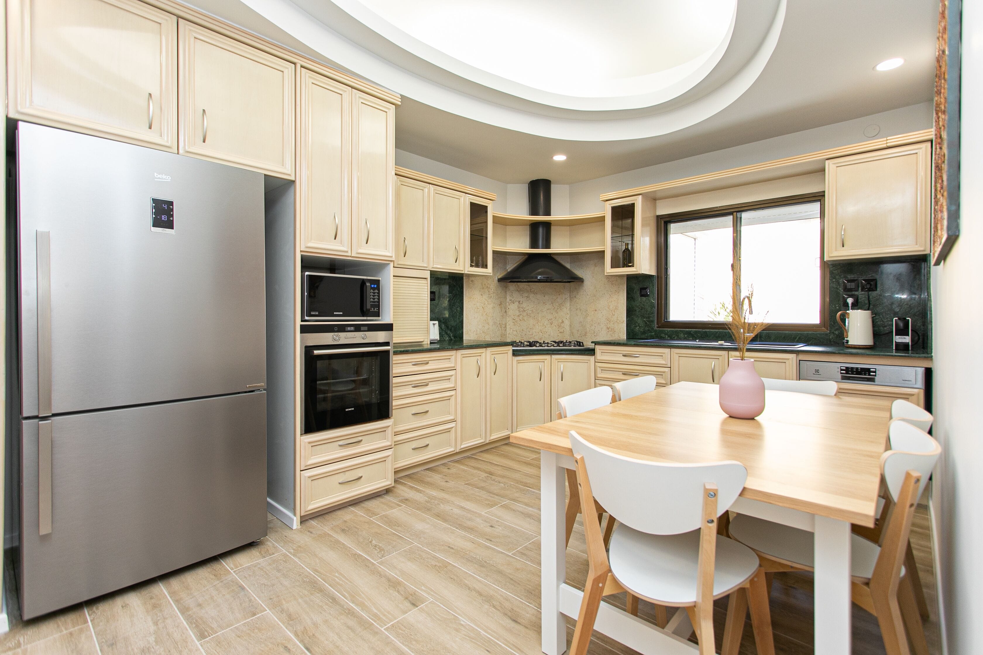 A modern kitchen with a stainless steel refrigerator, built-in oven, microwave, and stove. There is a dining table with chairs and a vase on the table.