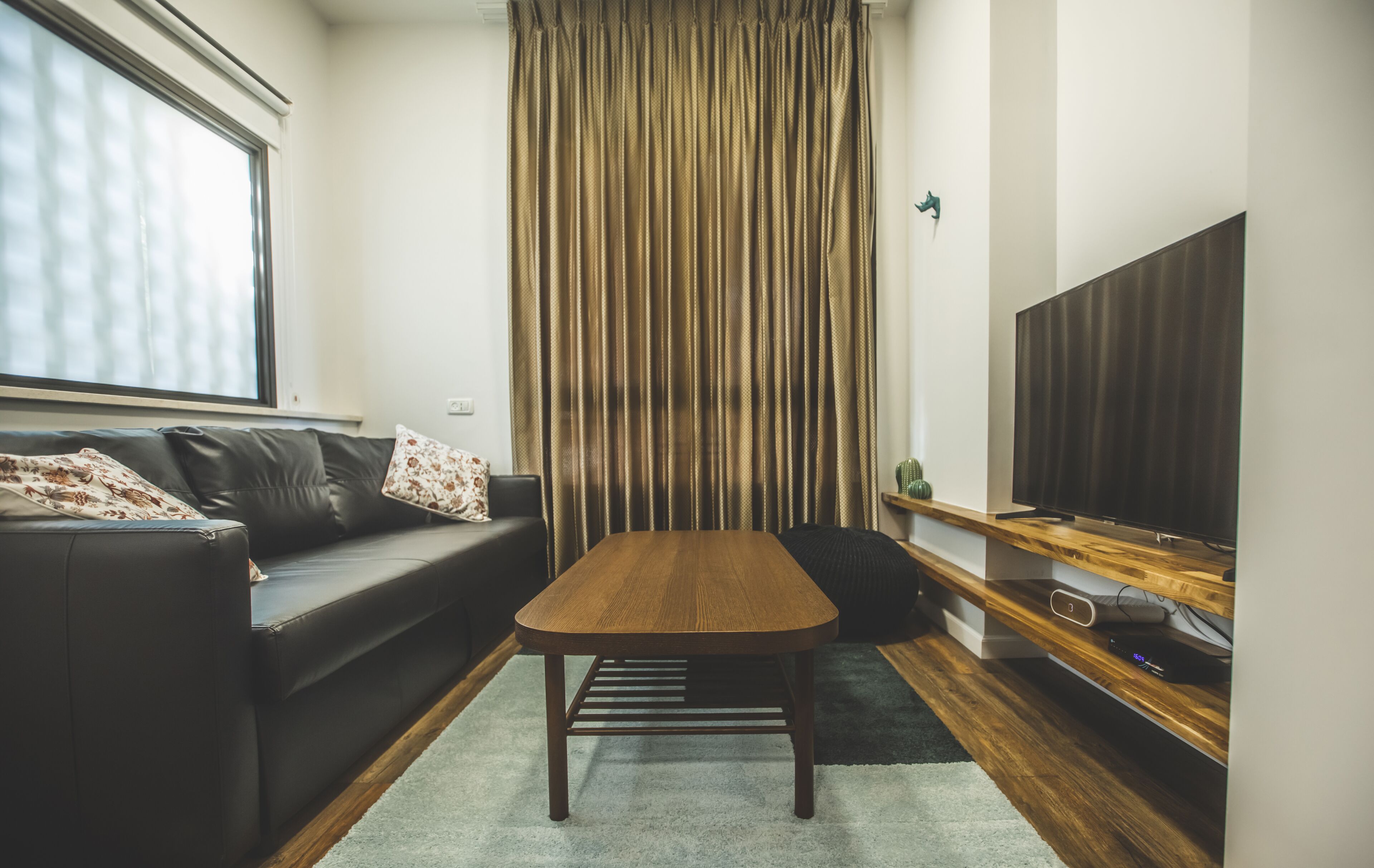 A modern living room with a wooden coffee table, a black leather sofa, and a television on a wooden stand.