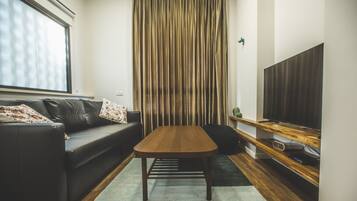 A modern living room with a wooden coffee table, a black leather sofa, and a television on a wooden stand.
