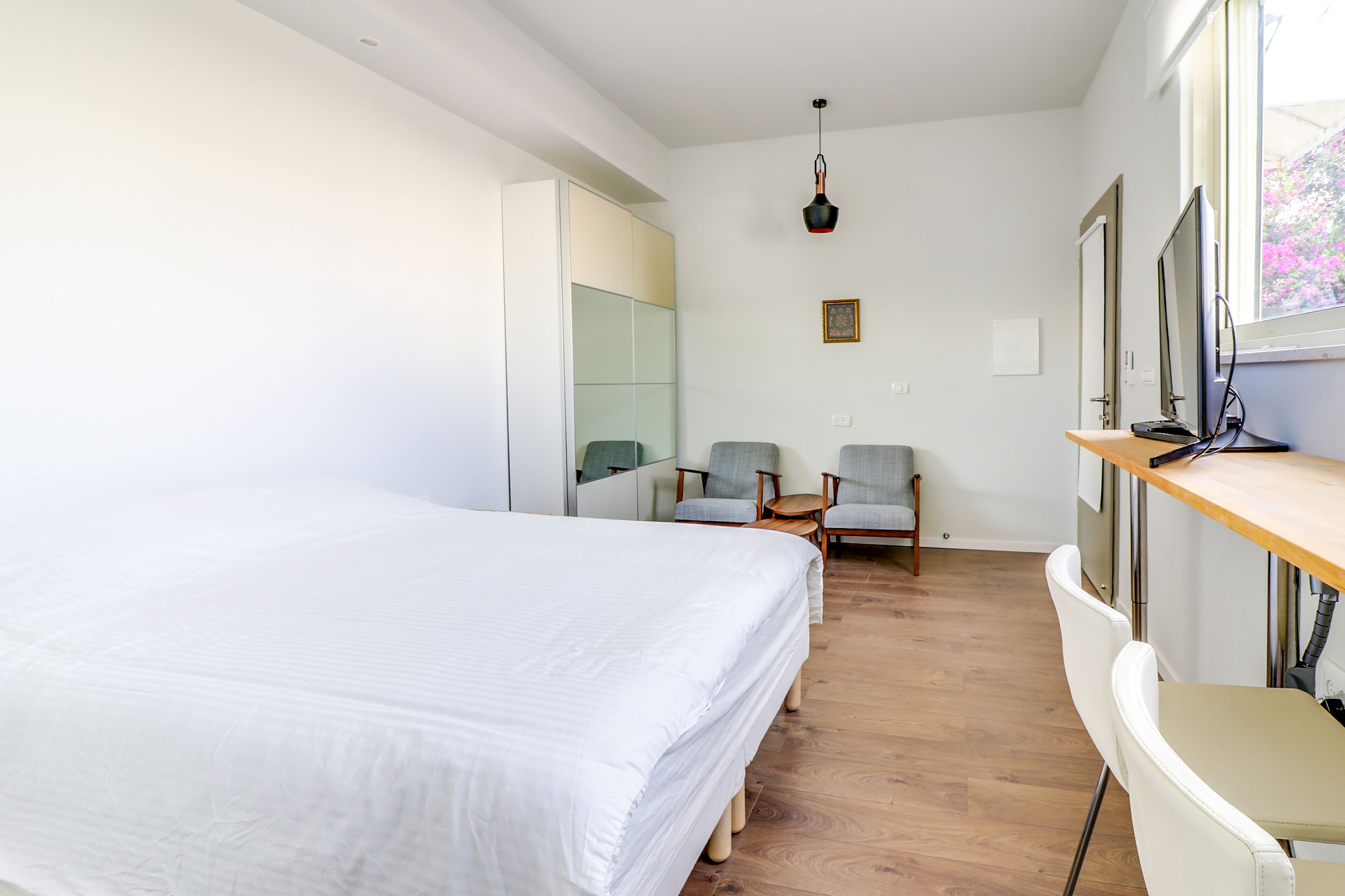 A modern hotel room with a large bed, a desk, two chairs, and a large window.
