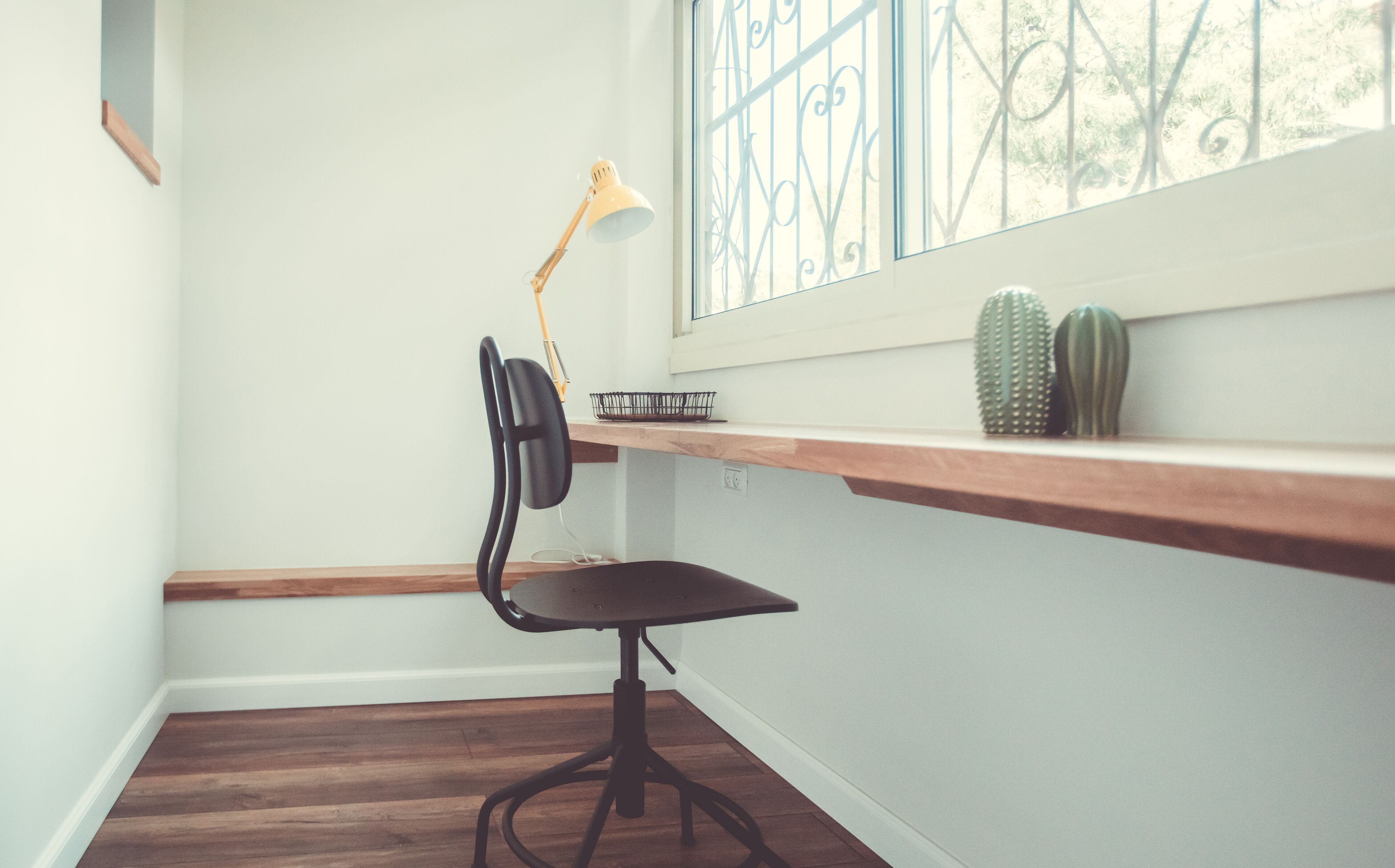 Een hoekwerkplek met een bureau, stoel en een raam met decoratieve ijzeren spijlen.