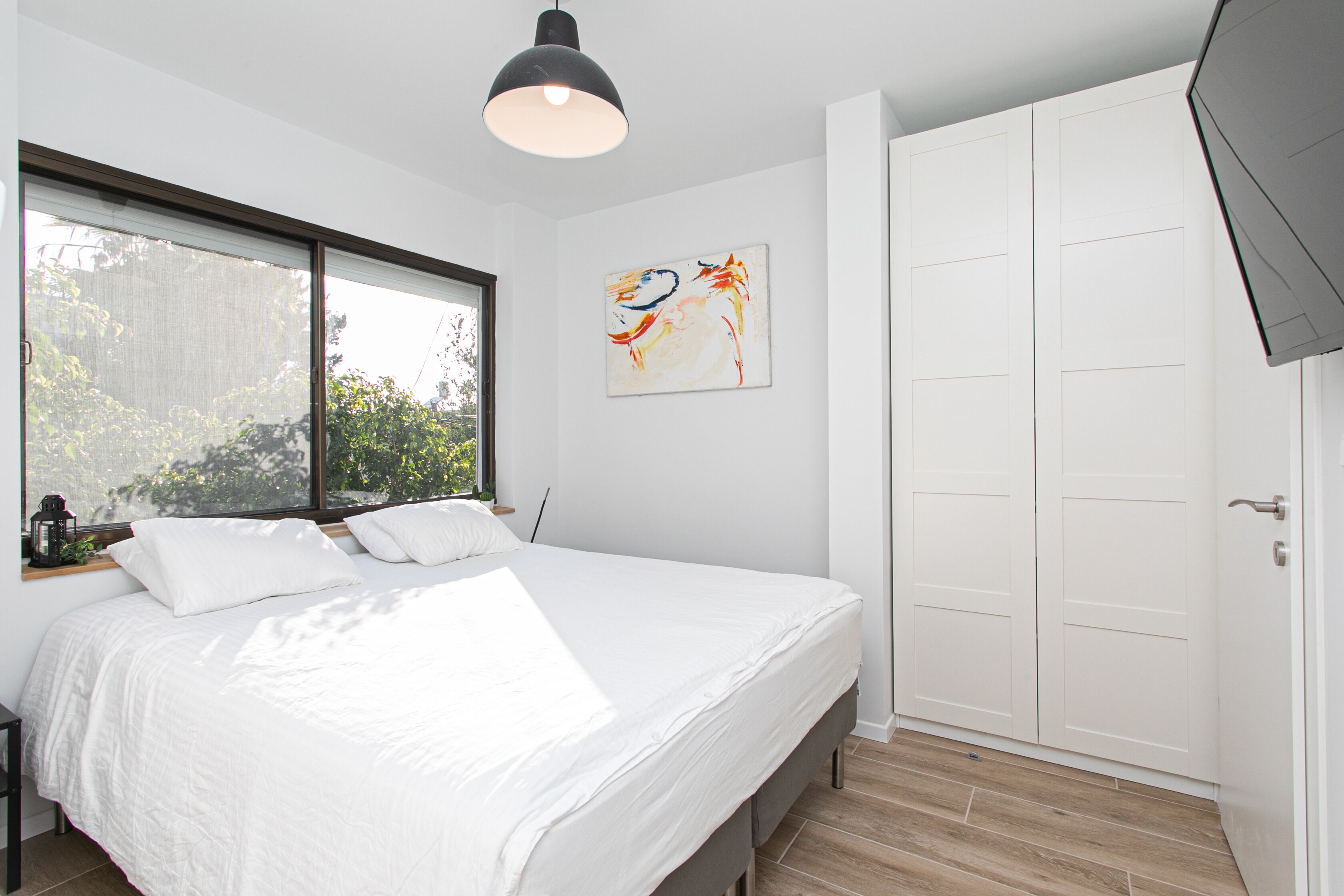 A bedroom with a large bed, a window, a painting, and a wardrobe.