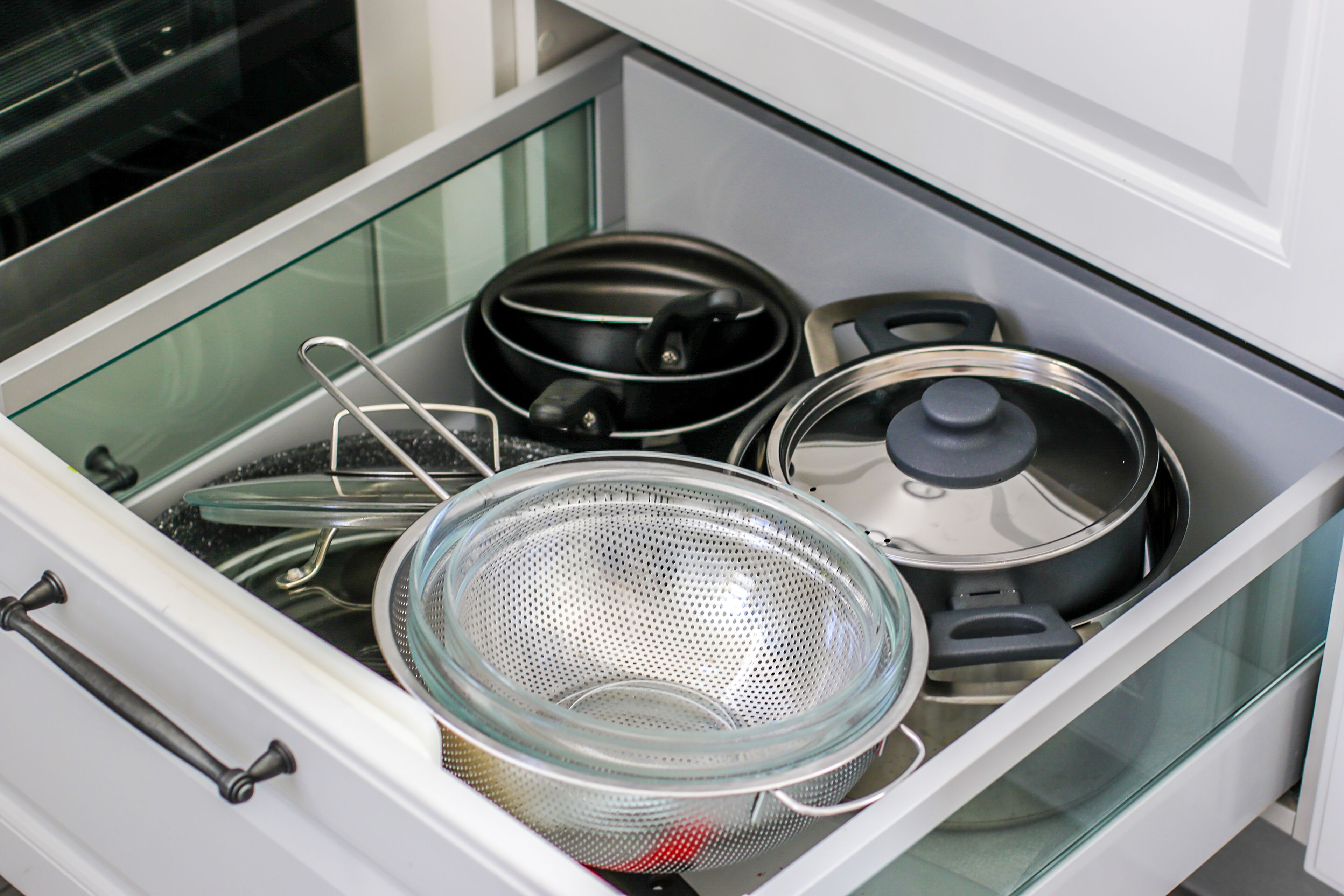 A kitchen drawer with a colander, a frying pan, and a pot.