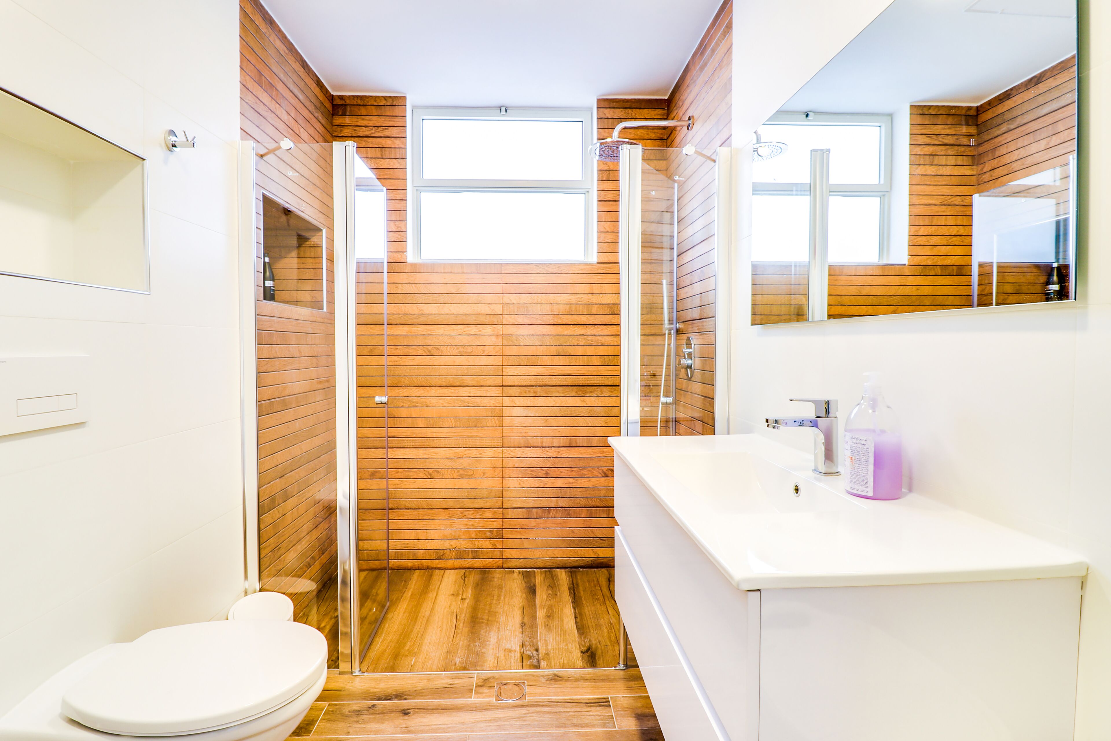 A bathroom with a wooden wall, a glass shower enclosure, a white sink, and a toilet.