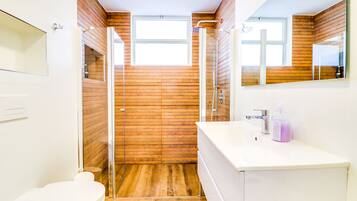 Un baño con pared de madera, cabina de ducha con vidrio, lavamanos blanco y un inodoro.
