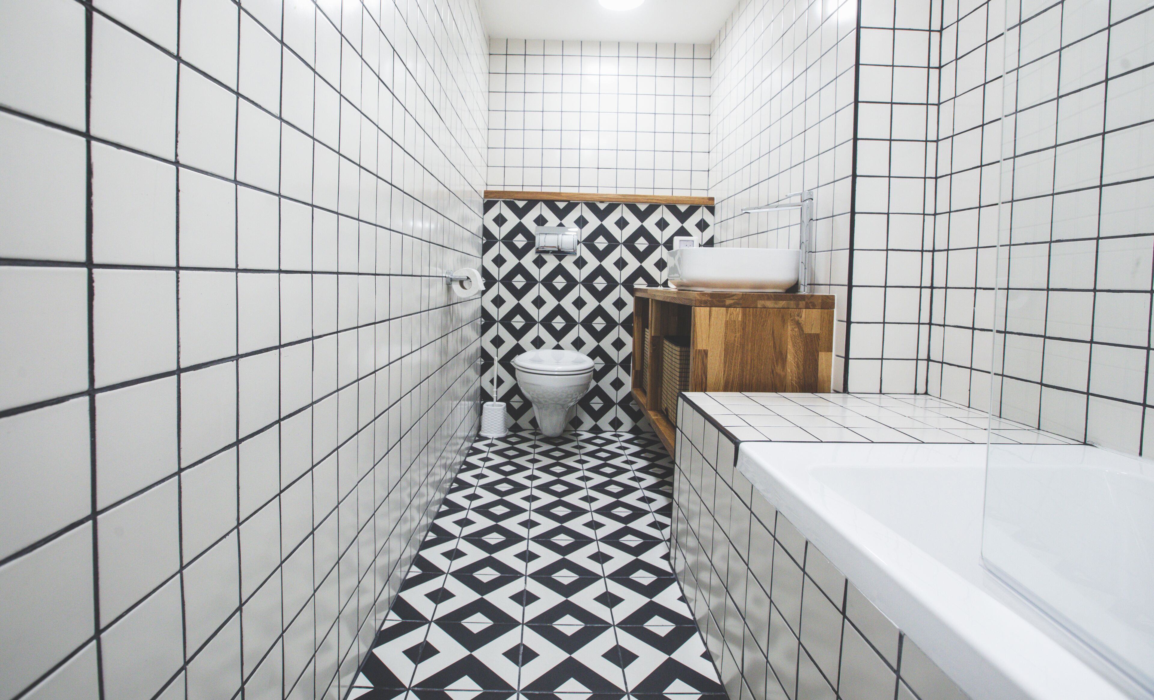 Et aflangt badeværelse med et geometrisk gulvmønster, et toilet og et badekar.