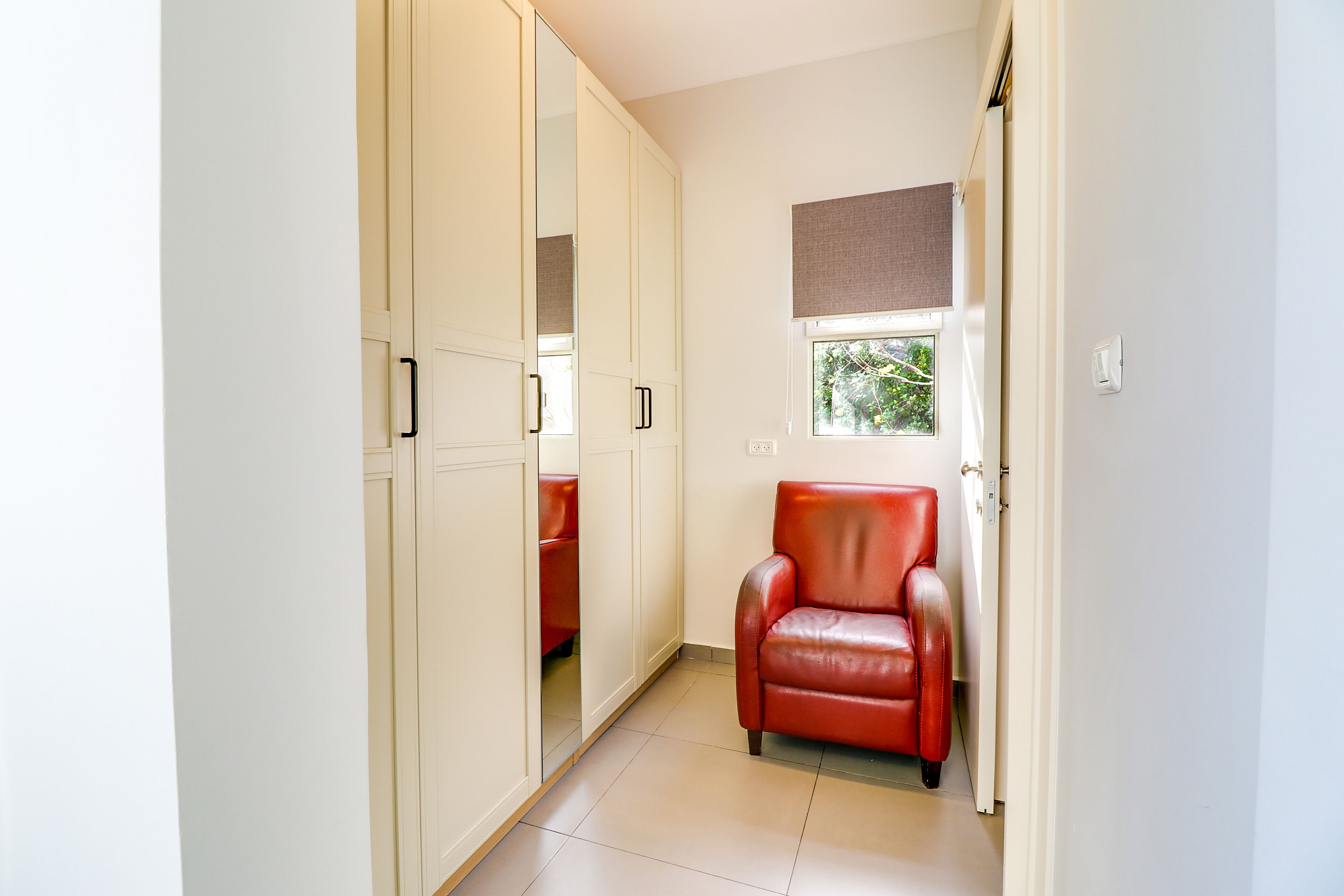 A hallway with a red chair, a wardrobe, and a window with a view of greenery.