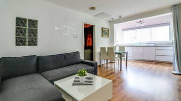A modern living room with a grey sofa, a white coffee table with a plant, and a dining area with a table and chairs.