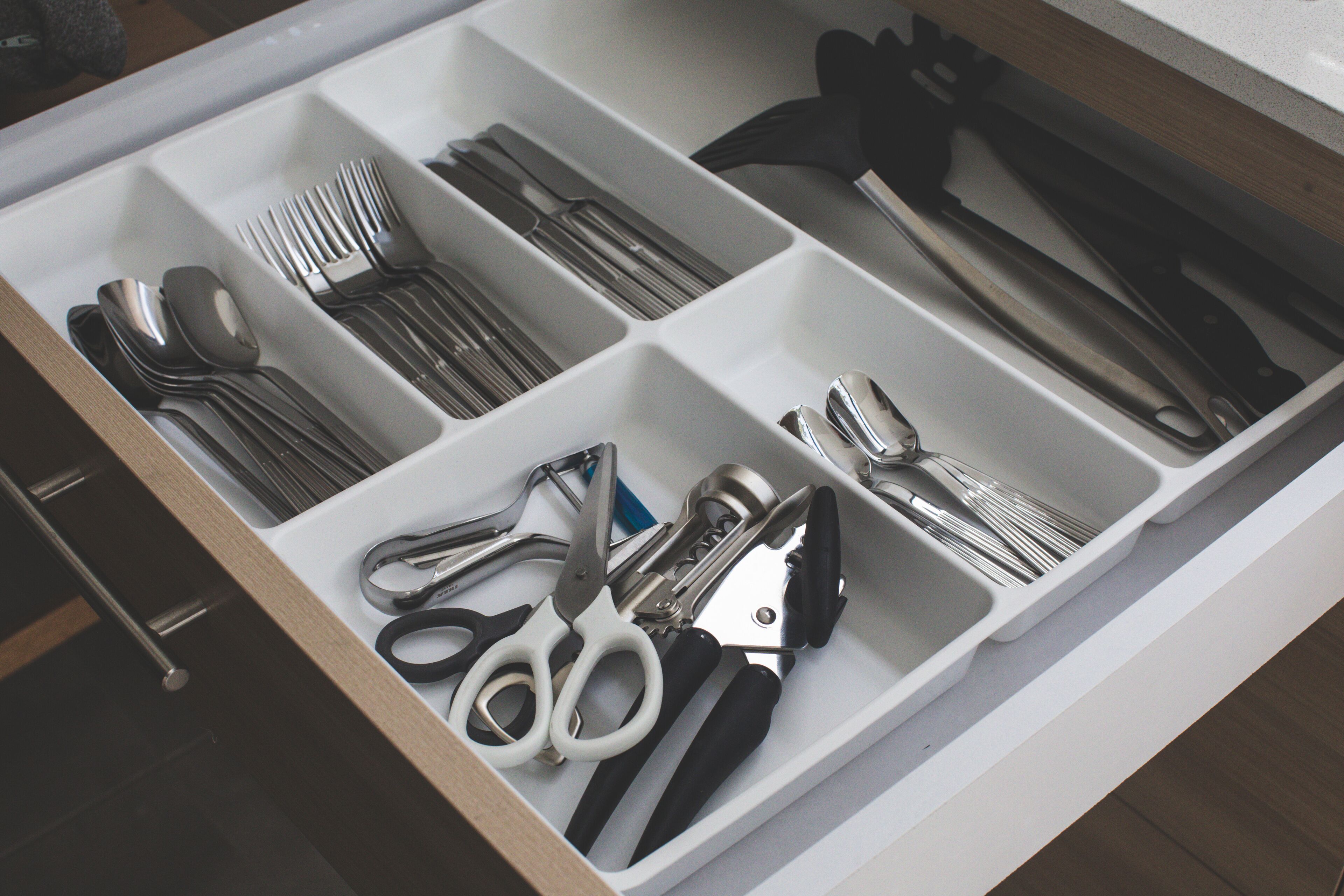 A drawer with compartments containing various kitchen utensils such as forks, knives, and scissors.