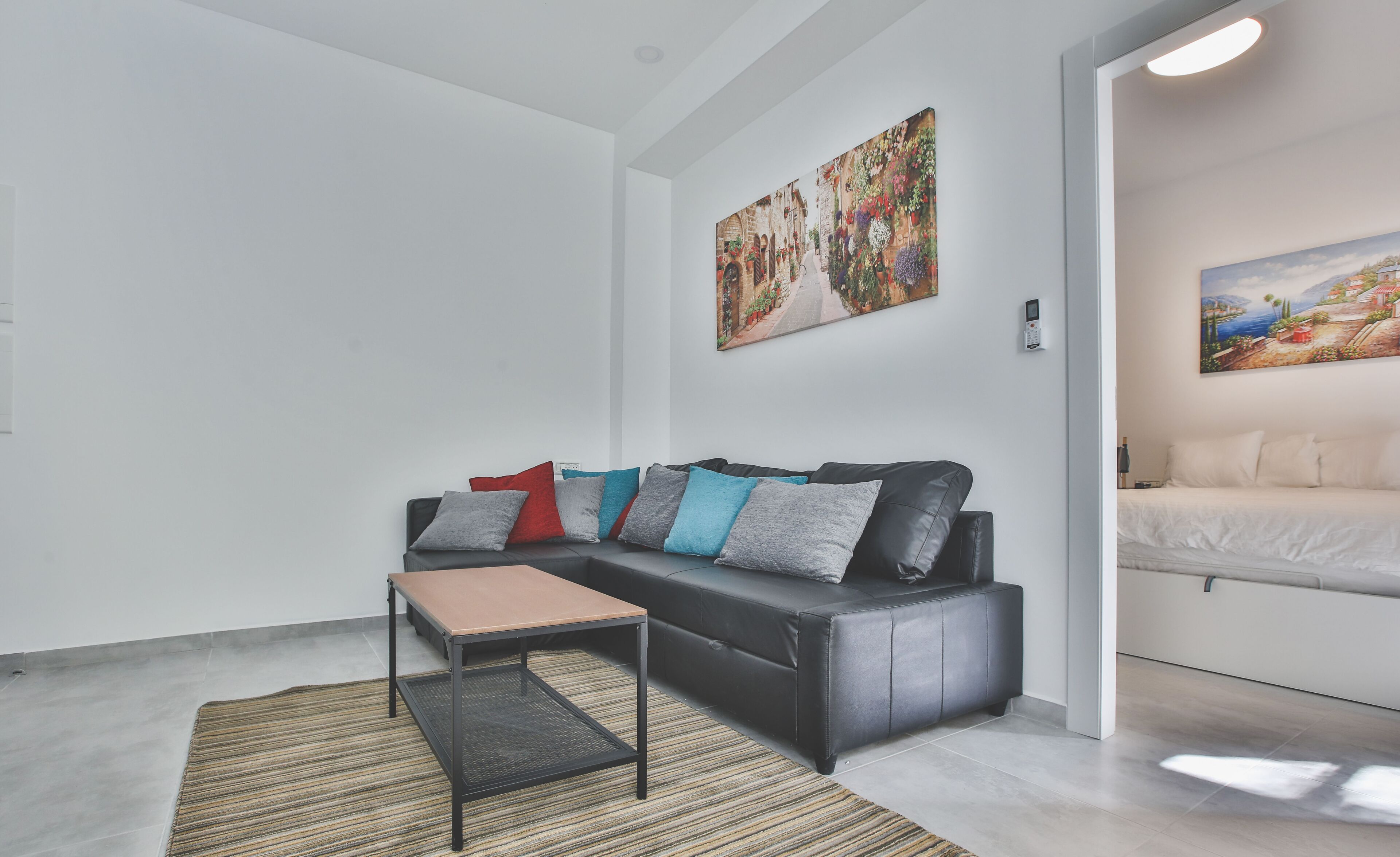 Een moderne woonkamer met een zwarte leren bank, een klein houten tafeltje en een gestreept tapijt.
