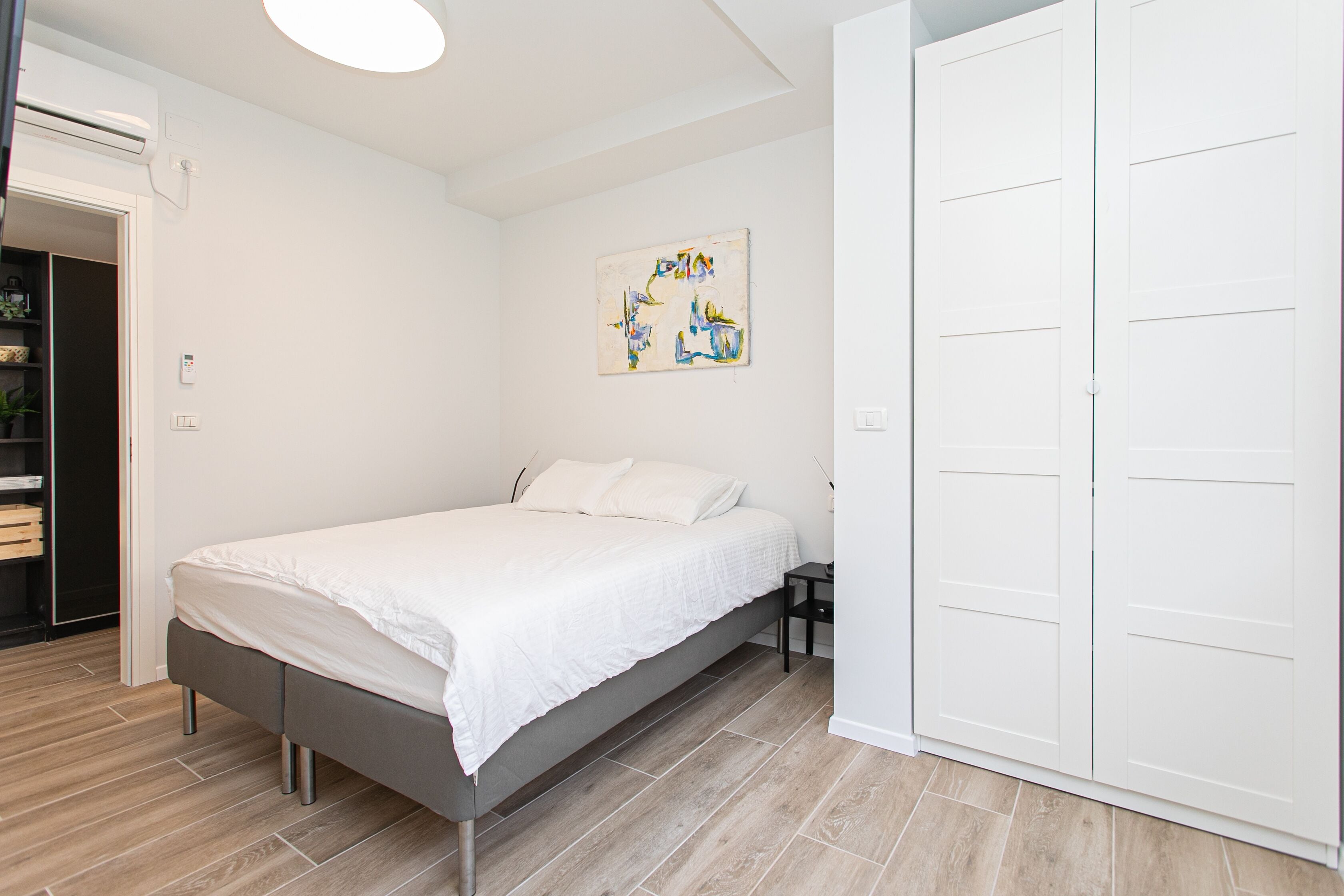 A bedroom with a bed, a wardrobe, and a painting on the wall.