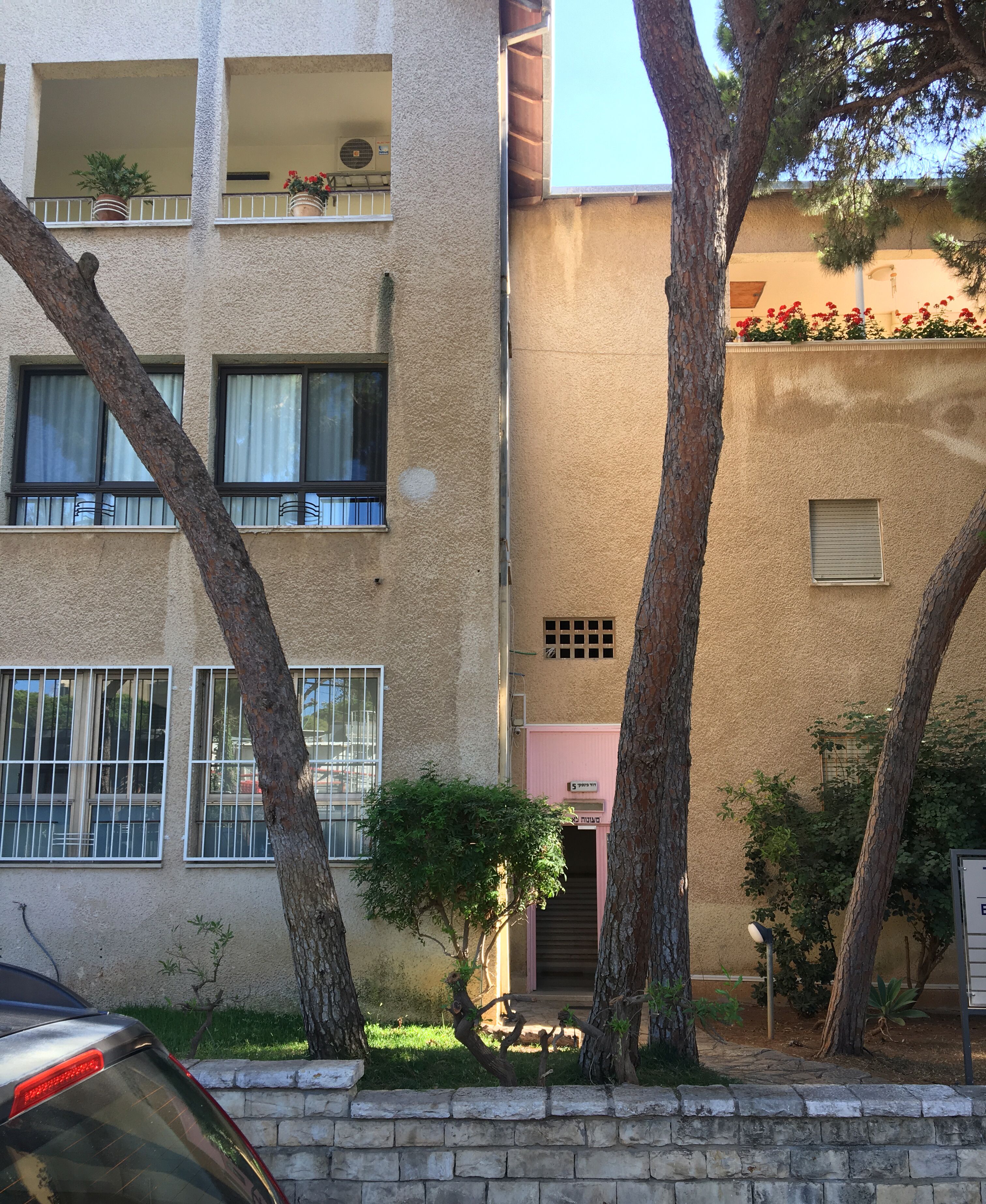 A multi-story building with balconies, a staircase leading to an entrance, and a parked car.