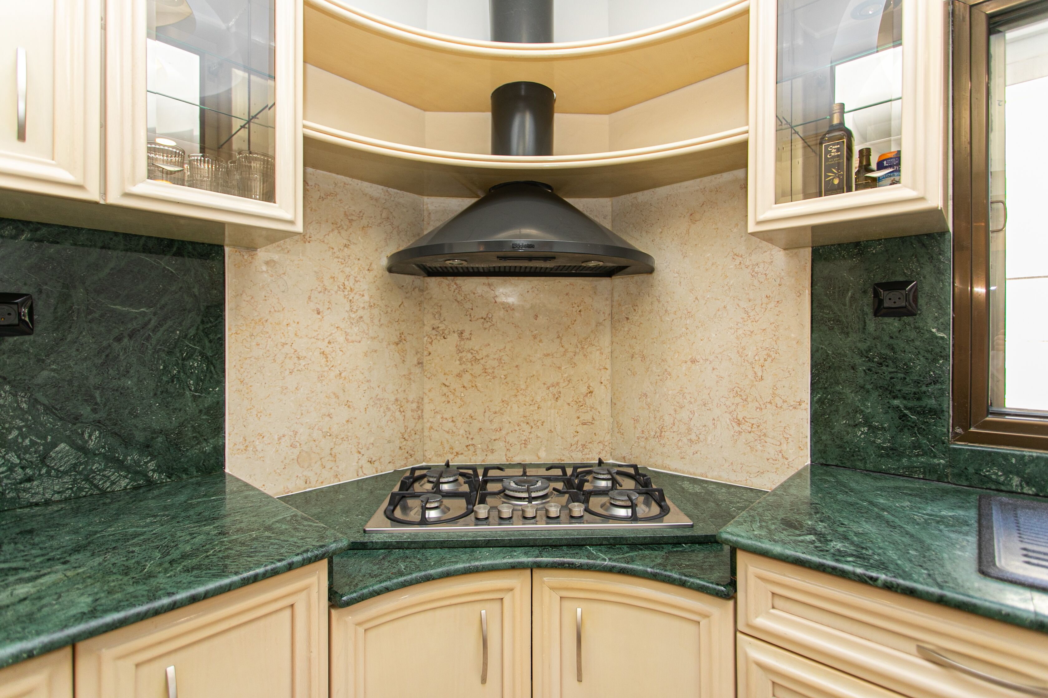 A kitchen with a gas stove, beige cabinets, and a marble countertop.