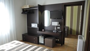 Habitación de hotel con cama, cómoda, espejo, televisor y refrigerador pequeño.