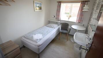 A small, single-bed room with a bedside table, a chair, a round table, and a sink.