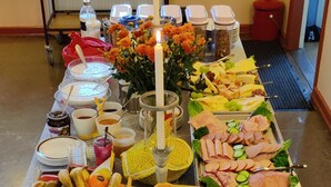 A buffet table with various food items, including fruits, meats, and breads, in a room with a window and a framed picture on the wall. - Hostel Rudbøl (Højer)