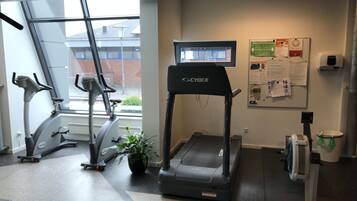 A gym with treadmills, stationary bikes, and a wall-mounted screen.