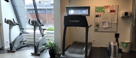 A gym with treadmills, stationary bikes, and a wall-mounted screen.