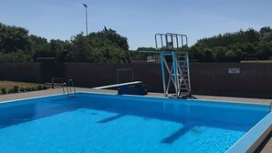 A rectangular swimming pool with a diving board and ladder, surrounded by a tiled deck and a low wall. - Bredebro camping (Bredebro)