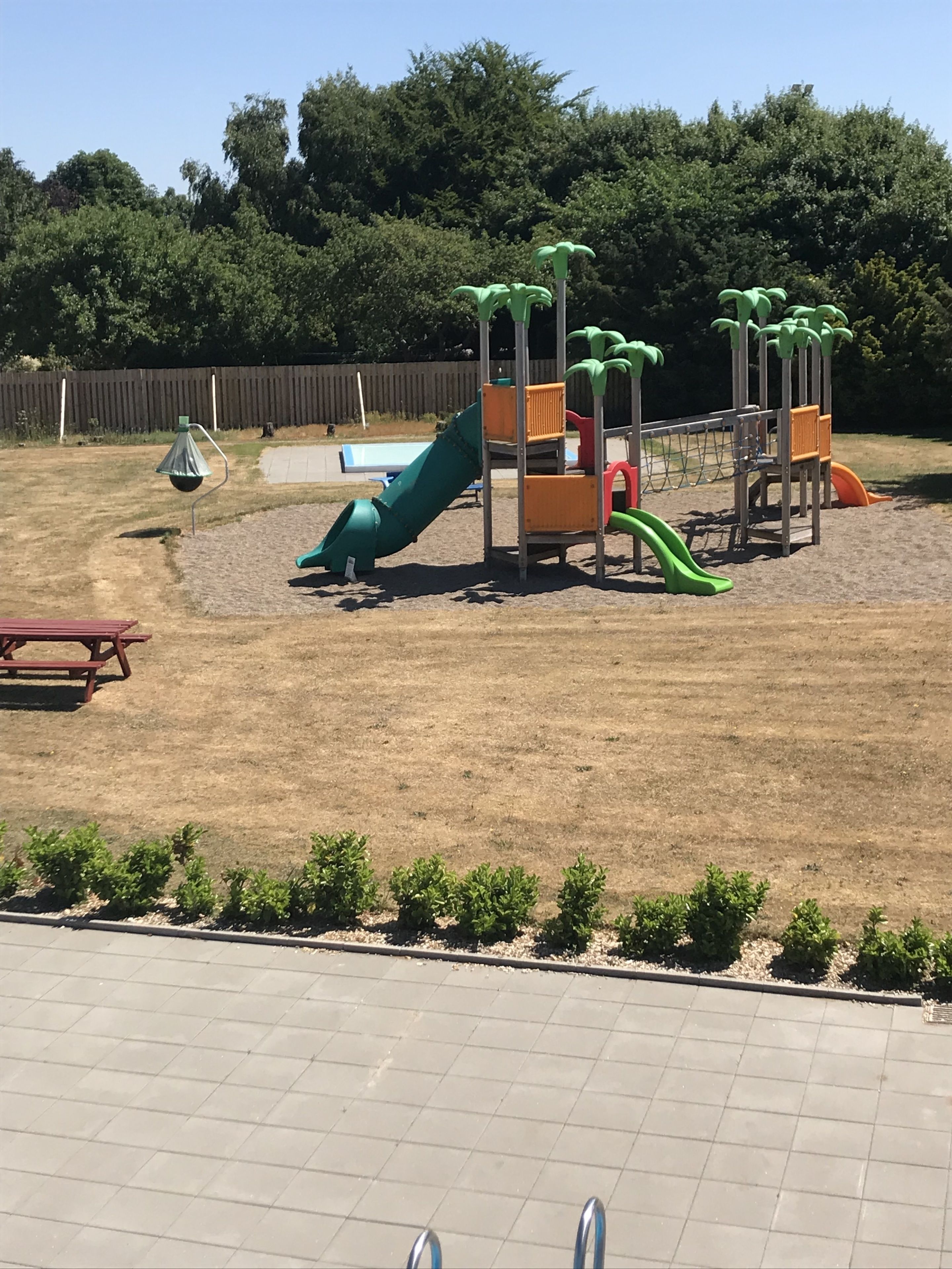 Un parque infantil con toboganes y estructuras para escalar, rodeado por una valla y una mesa de picnic.