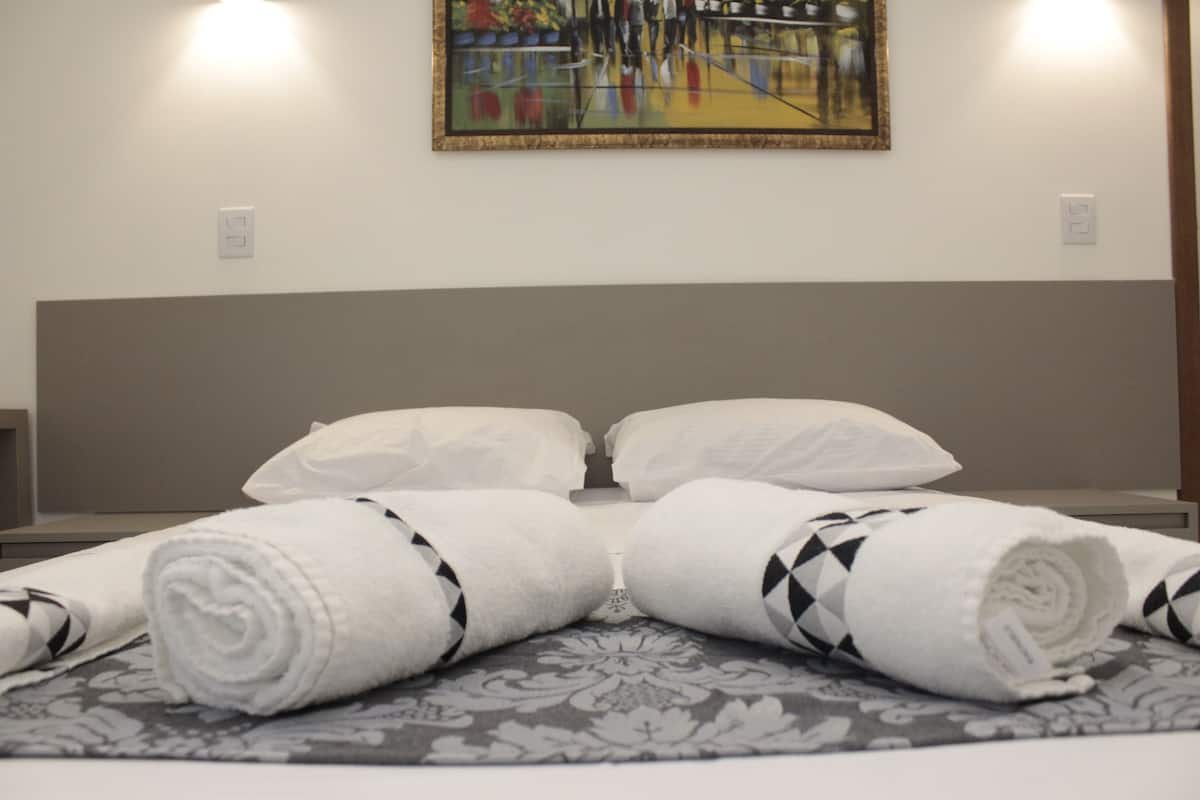 A hotel room with a bed, two white pillows, and two rolled towels with a black and white pattern.