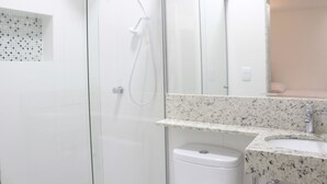 A bathroom with a glass shower enclosure, a white toilet, a sink with a granite countertop, and a mirror above the sink. - Hotel Hellyu's (Nucleo Bandeirante)