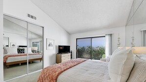 Een slaapkamer met een groot bed, een televisie, een dressoir en een schuifdeur naar een balkon.