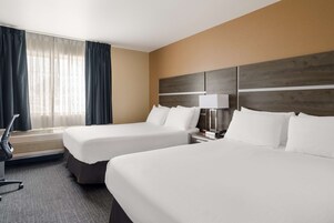 Habitación de hotel con dos camas, un escritorio, una silla, una lámpara y una ventana con cortinas.